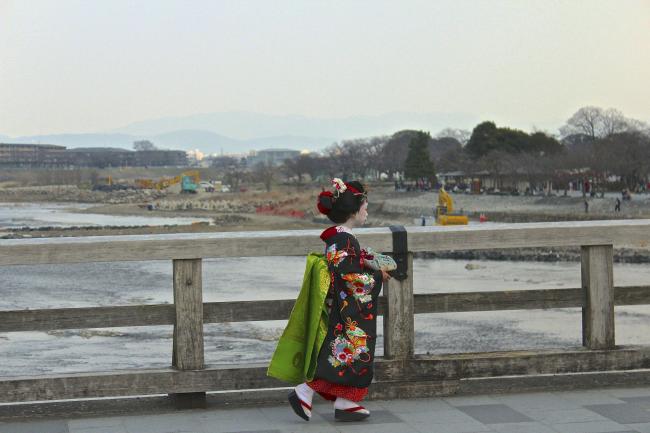 A girl wearing  kimono while crossing a bridge.