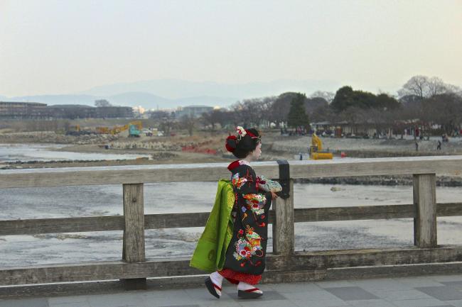 A girl wearing kimono while crossing a bridge.