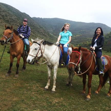 Students horseback riding in a grassy field.