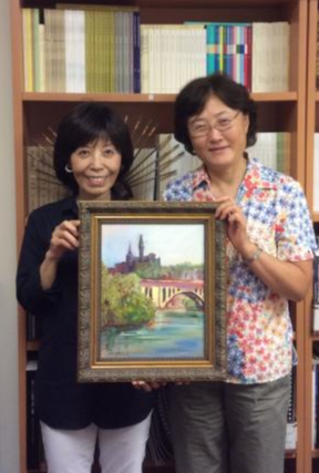 Professor Yu with a colleague holding up a painting of Georgetown University.
