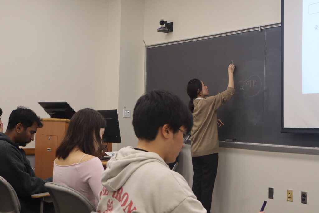 Professor at blackboard, students sitting in classroom